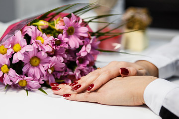 Obraz na płótnie Canvas Hands of a woman with red manicure on nails and flowers against white background