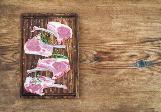 Rack of Lamb with rosemary and spices on rustic chopping board over old wooden background.