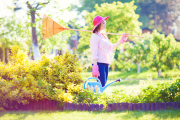 Young cheerful woman wearing hat and gloves holding rakes in the garden, Gardening concept