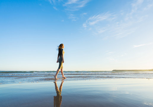 Young woman in dress walk on the beach at sunset time.