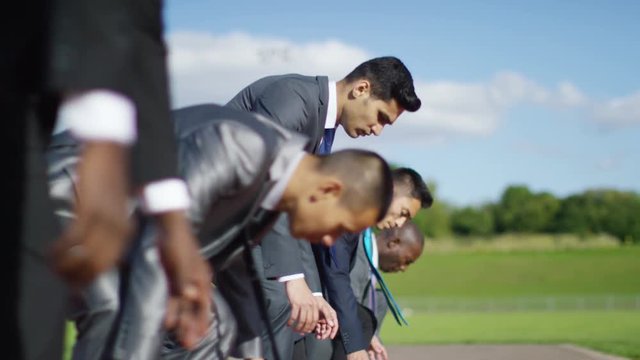  Competitive businessmen at running track line up at starting line before race