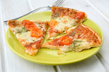 portions of pizza with cheese and tomato on green plate on wood
