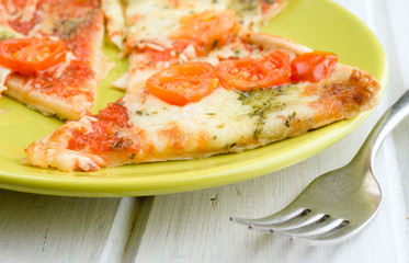 portions of pizza with cheese and tomato on green plate on wood