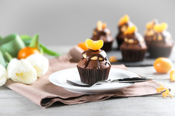 Tasty cupcake with slice of mandarin and chocolate on a plate over light wooden background