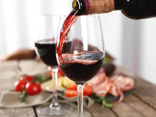 Rolgordijnen Pouring red wine into glass on wooden table closeup © Africa Studio