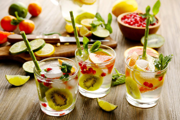 Refreshing cocktails with ice, mint, pomegranate seeds and slices of fruits on wooden background