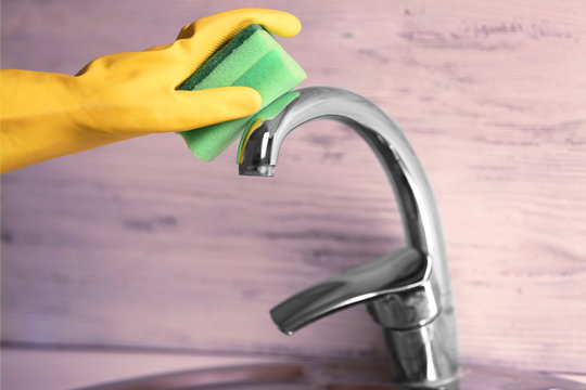 Female hand with sponge cleaning a tap in the kitchen