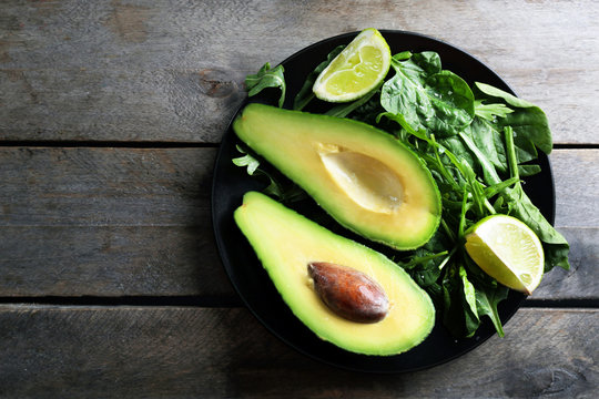 Sliced avocado with lime, spinach and arugula on black plate