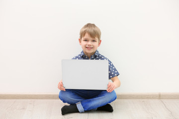 Little boy with laptop on white wall background