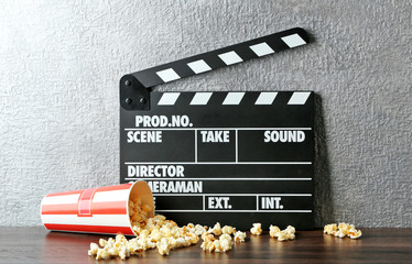 Movie clapper and popcorn against grey wall background