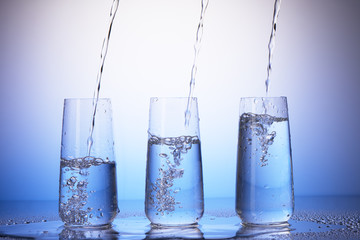 Drinking glasses with reflection in drops. Water pouring