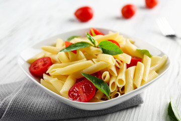 Plate of pasta with cherry tomatoes and basil leaves on table closeup