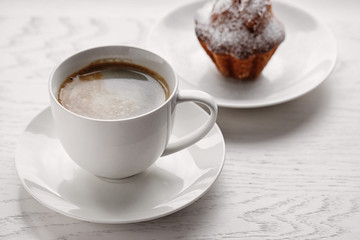 Cup of coffee with cake on light wooden background
