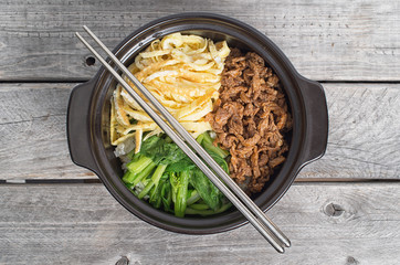 Korean cuisine, egg and  beef Bibimbap in  a clay pot on a woode