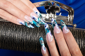 Beautiful female hands with blue flower manicure holding the black handbag. - 110658297