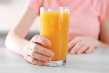 Female hand holding glass of orange juice on wooden table closeup