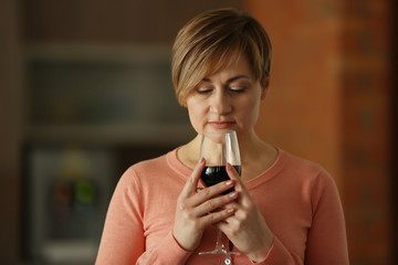 Beautiful middle-aged woman tasting red wine, indoors