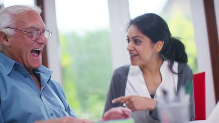  Cheerful home support worker showing elderly man how to use a computer