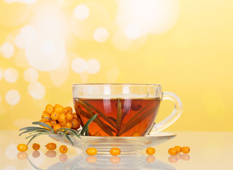 Bunch  sea buckthorn and cup with beverage from her abstract yellow background.