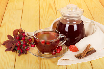Jug and cup of rosehip drink, vanilla sticks on a background  light wood.