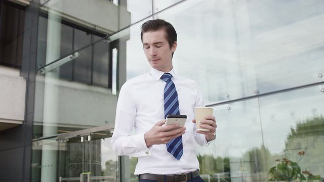  Young businessman looking at mobile phone as he walks outside office