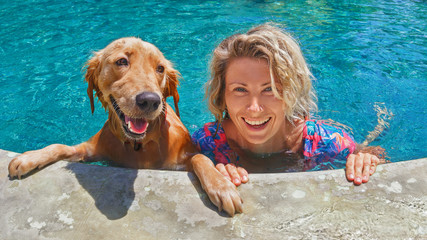 Funny portrait of smiling woman playing with dog and training golden retriever puppy in blue...
