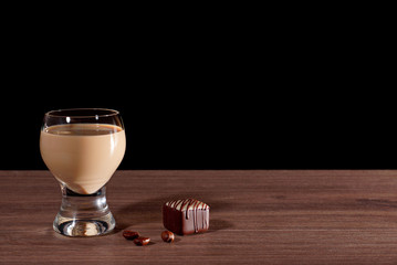 Glass with liquor, candy and coffee beans on a black background - 110670891