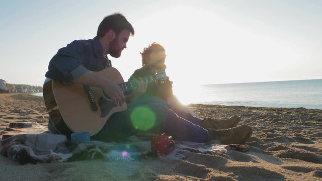 Young loving couple playing guitar on the beach, 4k