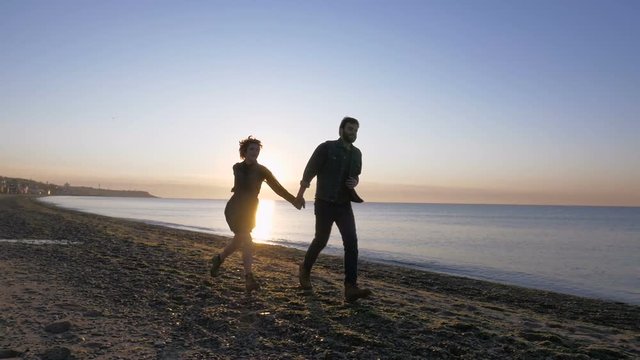 happy loving couple running on beach during sunrise or sunset, slow motion