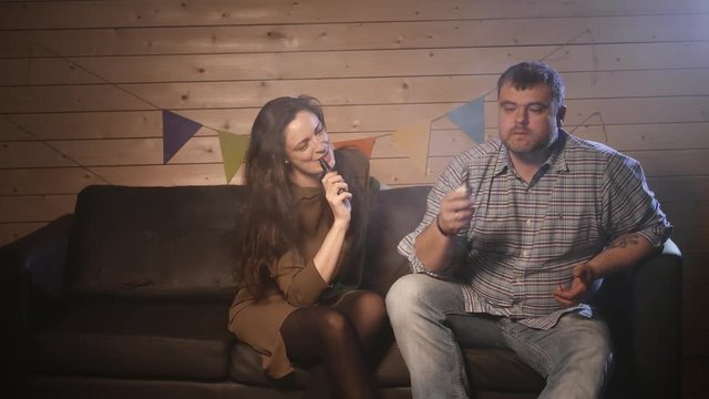 A couple vaping, inhaling and exhaling large clouds of smoke and having fun together.  Company of good friends. 4K UHD.