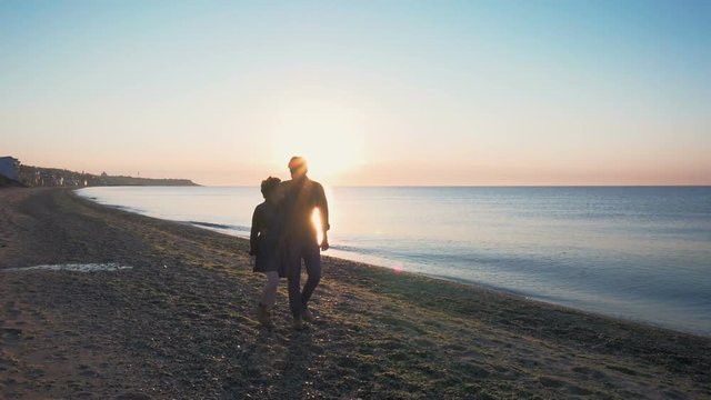 happy loving couple walking on beach during sunrise or sunset, slow motion