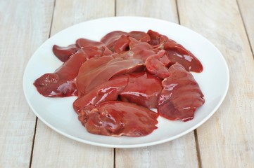 Raw liver on the white plate on the wooden background