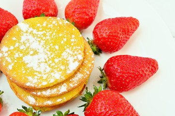 Pancakes on a white plate surrounded by ripe strawberries
