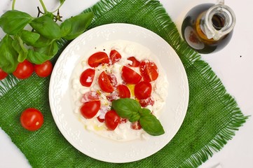 Salad from cherry tomatoes and cottage cheese with basil and olive oil