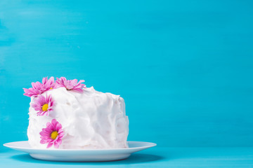 White creamy cake with flowers on the blue wooden background