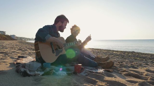 Young loving couple playing guitar on the beach, slow motion