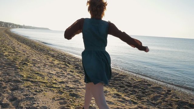 Young caucasian redhead girl running on beach during sunset or sinrise