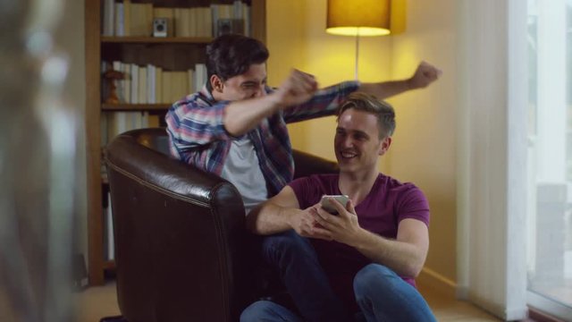  Attractive Young Gay Couple Relaxing At Home, Talking And Using Technology