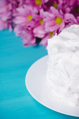 White creamy cake with flowers on the blue wooden background. Shallow depth of field.