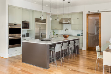 Kitchen interior with island and stainless steel appliances in new luxury home with lights on