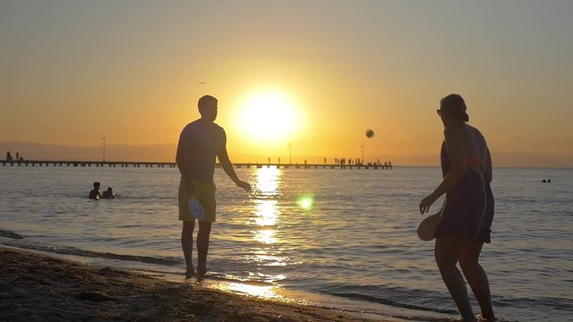 Slow motion shot of a couple playing racket ball on the beach at sunset.