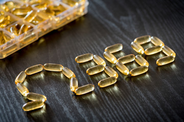 Omega 3-6-9 fish oil yellow softgels drawing omega 3-6-9  letters on wooden black table. Daily pill box.