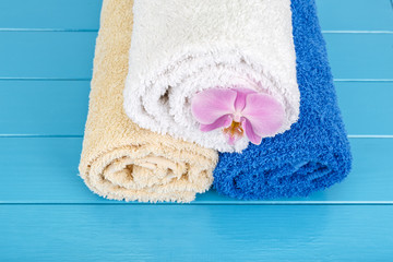 Obraz na płótnie Canvas Three twisted towels with orchid laying on a blue wooden backgro
