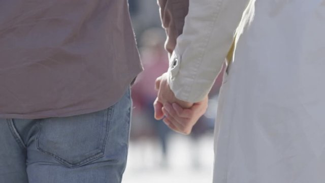  Romantic couple holding hands as they walk through crowded city