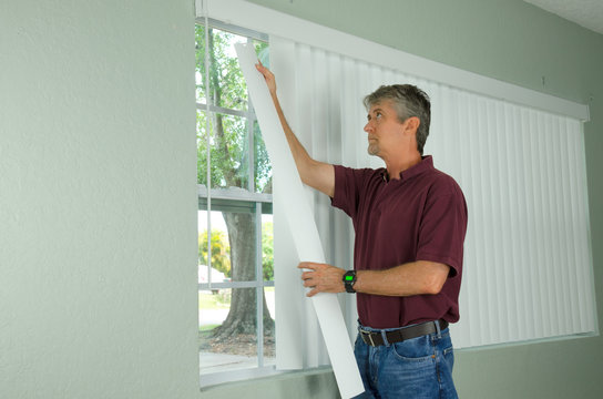 A Handy Man Home Repair Service Technician Or Home Owner Hanging White Vertical Blinds For The Window Treatment In A New House.