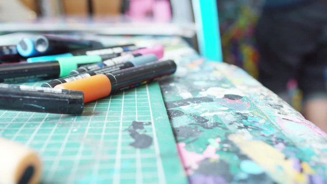 Close up of colored pens on artist's desk, with artist working in the background