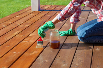 Woman applying protective varnish or wood oil on a patio wooden floor, house maintenance concept. Before and after effect