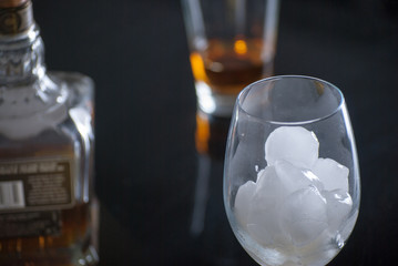 Whiskey Glass - Scotch Glass with ice cubes and Whiskey bottle with background and shinny reflection on bottom