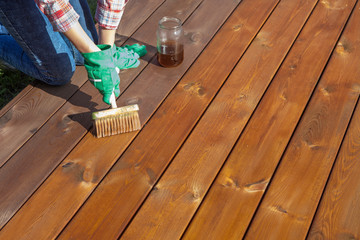 Woman applying protective varnish or wood oil on a patio wooden floor, house maintenance concept. Before and after effect