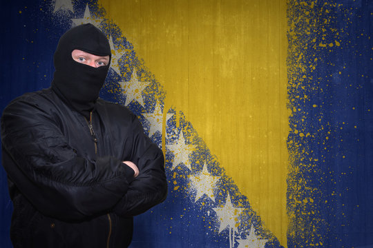dangerous man in a mask standing near a wall with painted national flag of bosnia and herzegovina